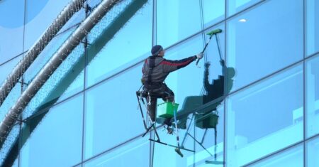 Homem usando equipamento de segurança limpando janelas de vidro.