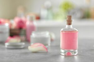 Frasco de vidro com fragrância rosa suave e pétala de rosa sobre mesa clara, ilustrando o tema perfume para criança