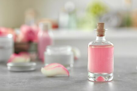 Como escolher perfume para criança com segurança Frasco de vidro com fragrância rosa suave e pétala de rosa sobre mesa clara, ilustrando o tema perfume para criança